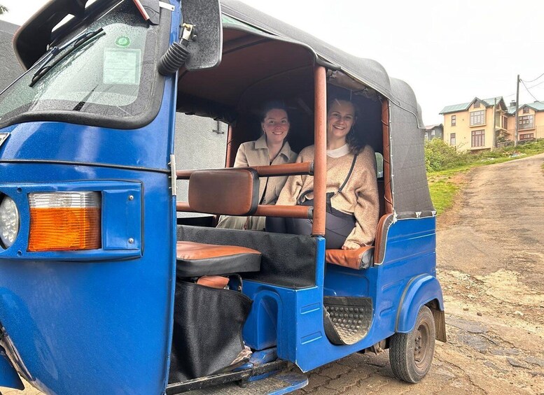 A blue auto-rickshaw with passengers, a dirt road, and houses in the background. 2