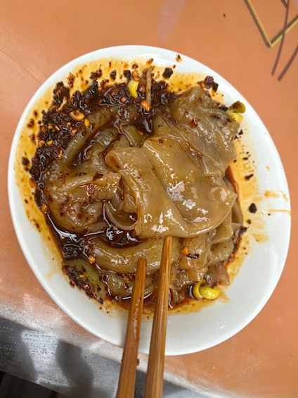 A plate of sliced vegetables in a dark sauce with chopsticks resting on it. 5