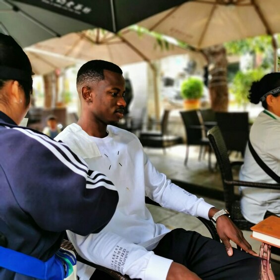 A person sitting at an outdoor cafe with a table, chairs, and umbrellas in the background. 5