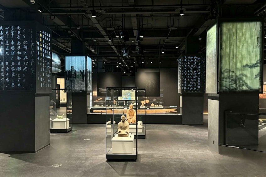 An indoor museum with exhibits, including a central display with a seated figure and surrounding panels with inscriptions. 2