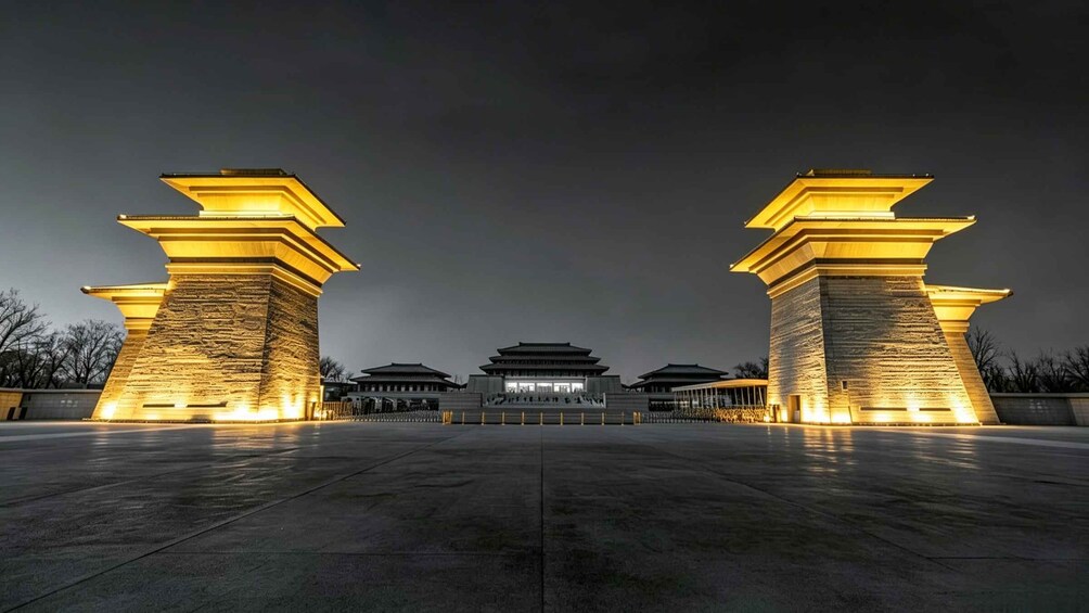 A night view of a traditional building with two illuminated stone pillars and a central gate. 1