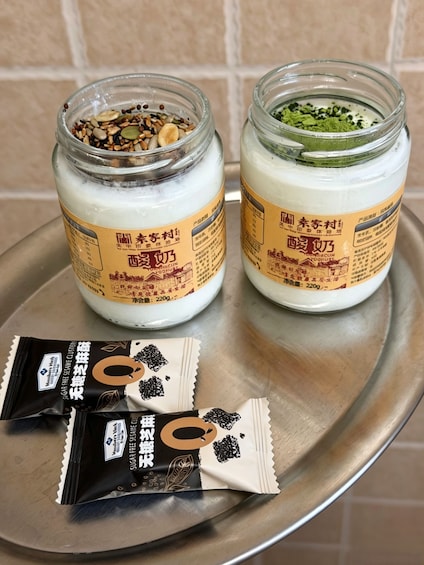 Two jars of yogurt with different toppings on a tray, and two packets of sugar-free sesame-flavored snacks beside them. 3