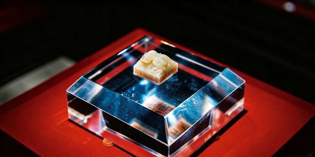 A clear glass cube with a small, white object on top, placed on a red surface. 3