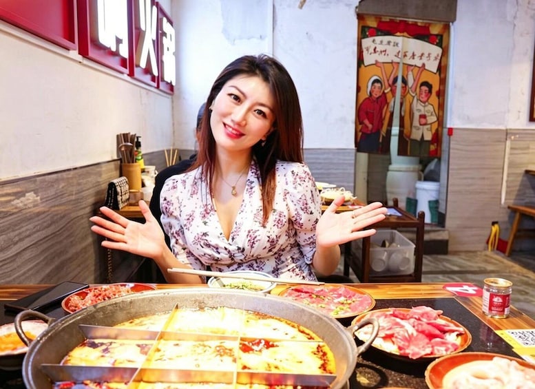 A person seated at a table with various dishes, including pizza and raw meat, in a restaurant with a red sign and a poster on the wall. 1