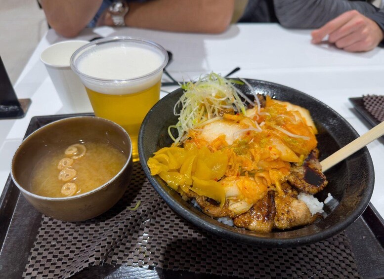 A bowl of ramen with a clear broth, a cup of beer, and a small bowl of soup. 3