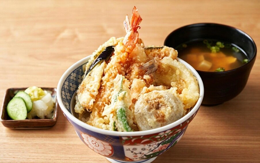 A bowl of tempura with shrimp, vegetables, and a side of soup and cucumber salad. 2