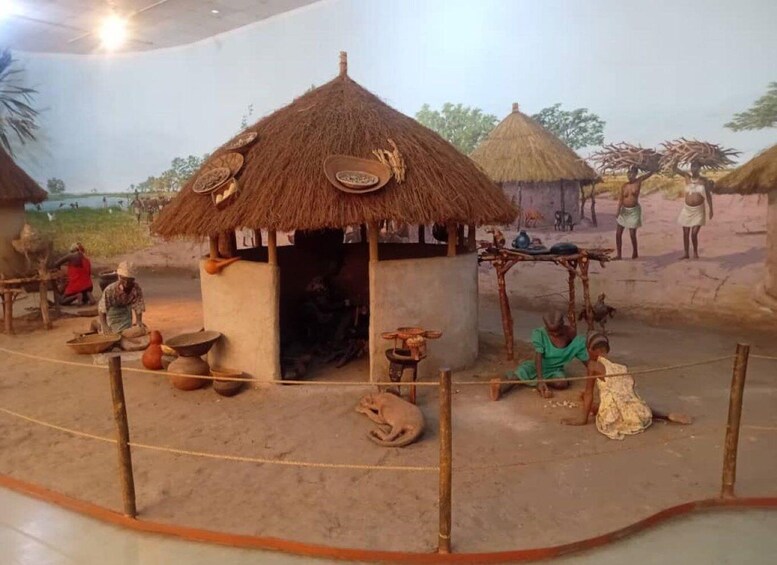 A model of a traditional village with huts, people engaged in daily activities, and a fenced area. 2