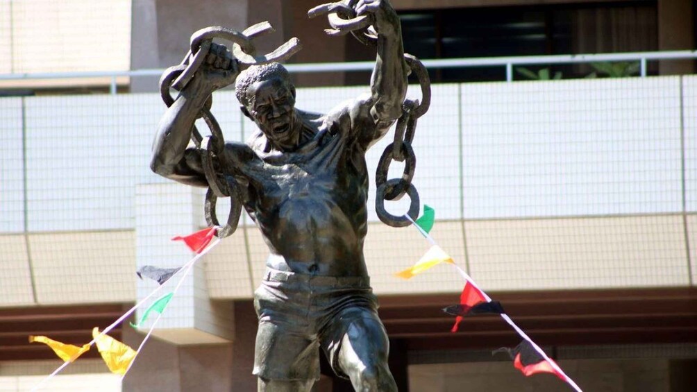 A statue of a muscular figure holding a chain, with colorful flags fluttering in the background. 1