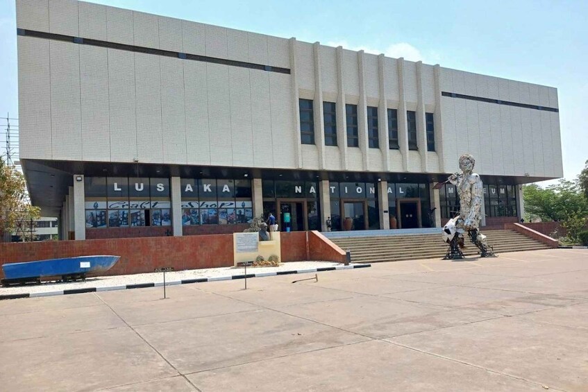 A modern building with the sign 'Lusaka National Museum' and a large statue in front. 4