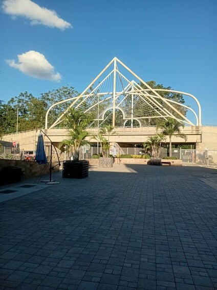 A modern architectural structure with a triangular roof and a paved plaza with palm trees. 3