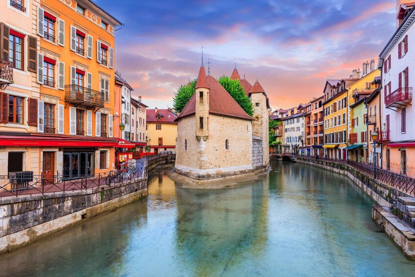 A canal with a tower, colorful buildings, and a sunset sky. 3
