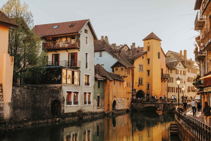 A canal with buildings on either side, a bridge, and people walking. 4
