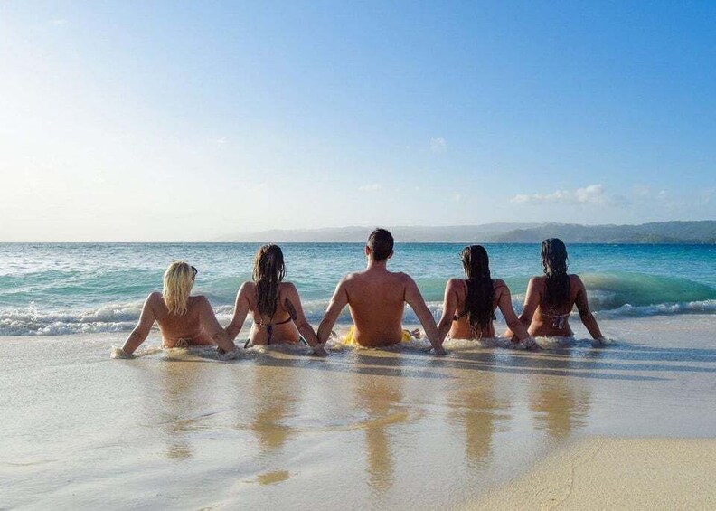 A group of people sitting on the beach facing the ocean. 3