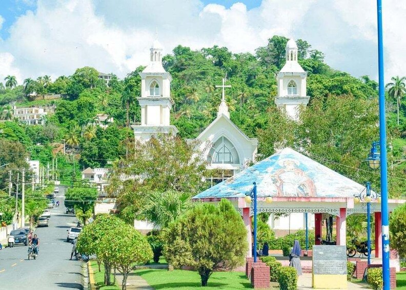 A white church with two towers, a gazebo, and a street with cars and people. 4