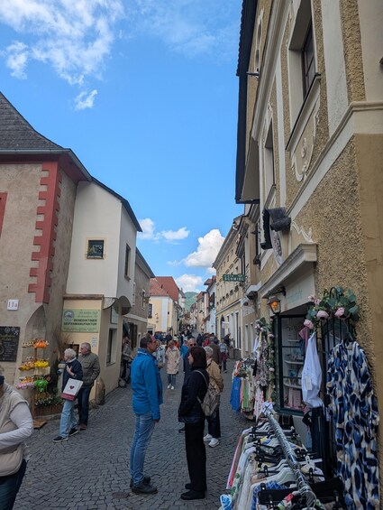 A cobblestone street lined with shops and buildings, a clear sky, and people walking. 3
