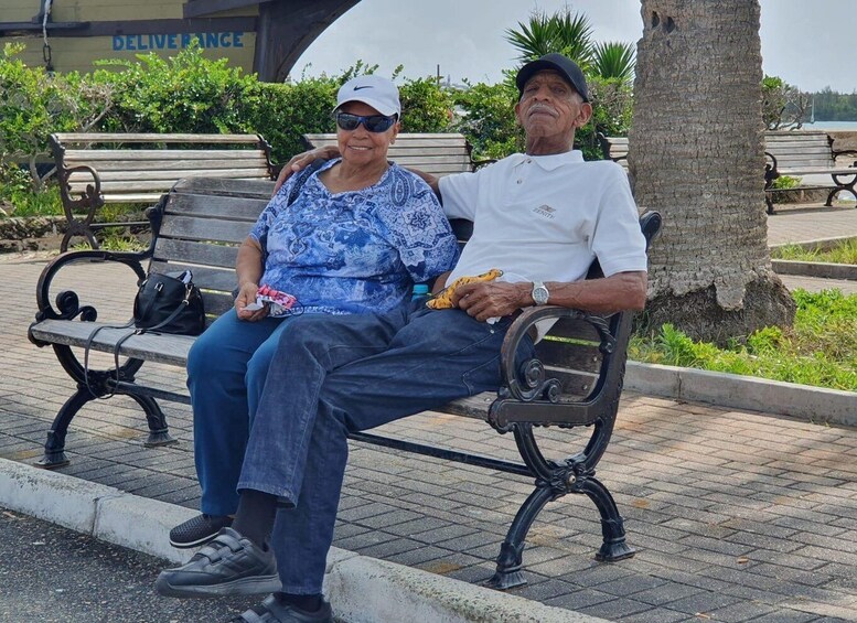 Two people sitting on a bench in a park with a tree and a building labeled 'DELIVERANCE' in the background. 3