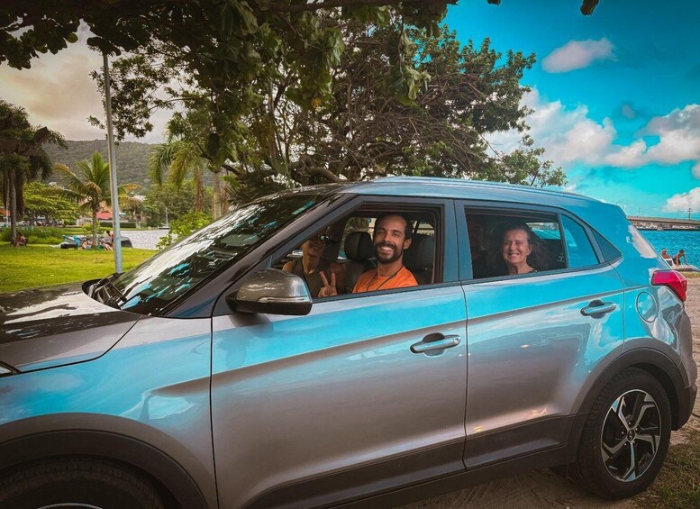 A light blue SUV parked in a sunny outdoor setting with lush greenery and a clear sky. 1
