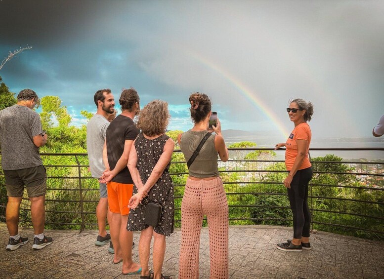 A group of people observing a rainbow over a landscape. 4