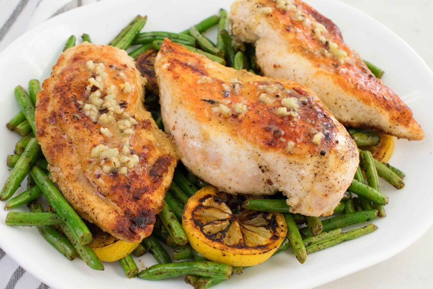 A plate of chicken breasts with green beans and lemon slices. 2