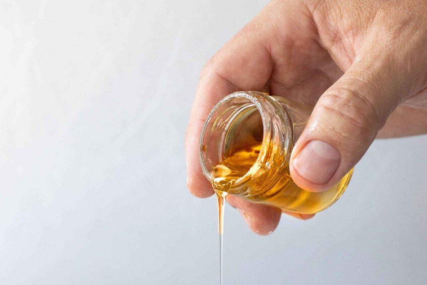 A hand holding a bottle of honey with honey dripping out. 3