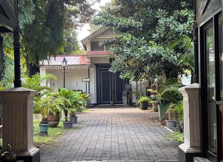 A paved courtyard with potted plants, a black door, and a building with a tiled roof. 2
