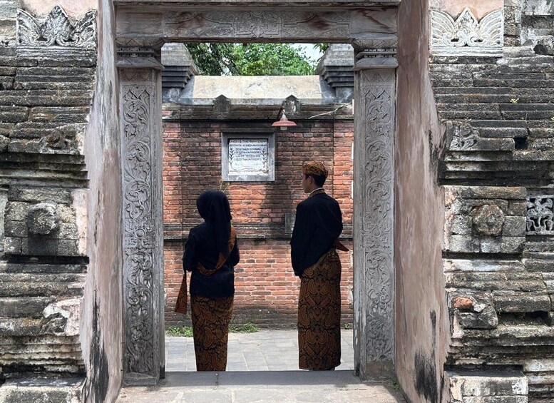 An ornate stone gateway with intricate carvings, leading to a brick structure with a plaque. 3
