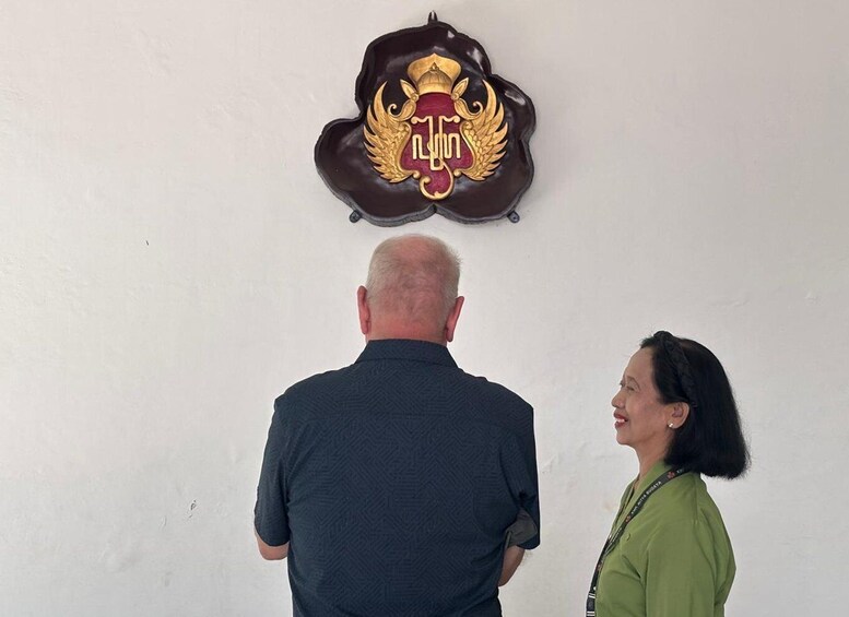 Two people looking at a wall-mounted emblem with a crown and wings. 1
