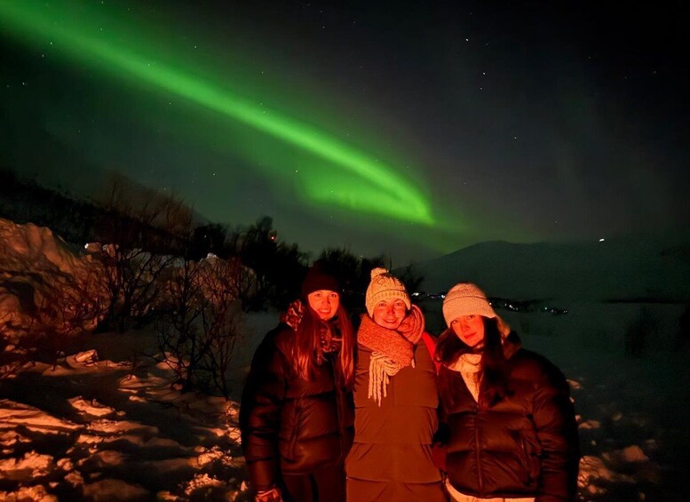 Three people standing in a snowy landscape with the Northern Lights in the sky. 2