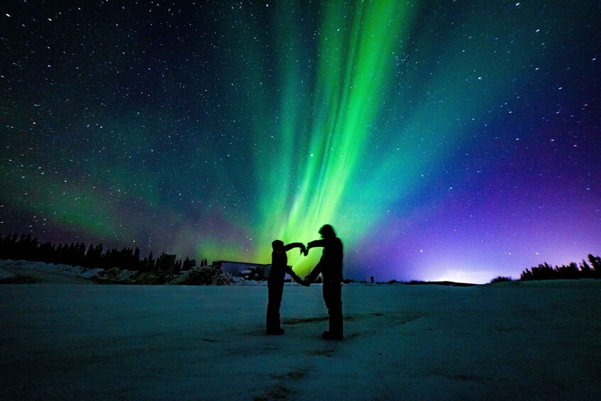 Two people forming a heart shape against a backdrop of the Northern Lights. 4