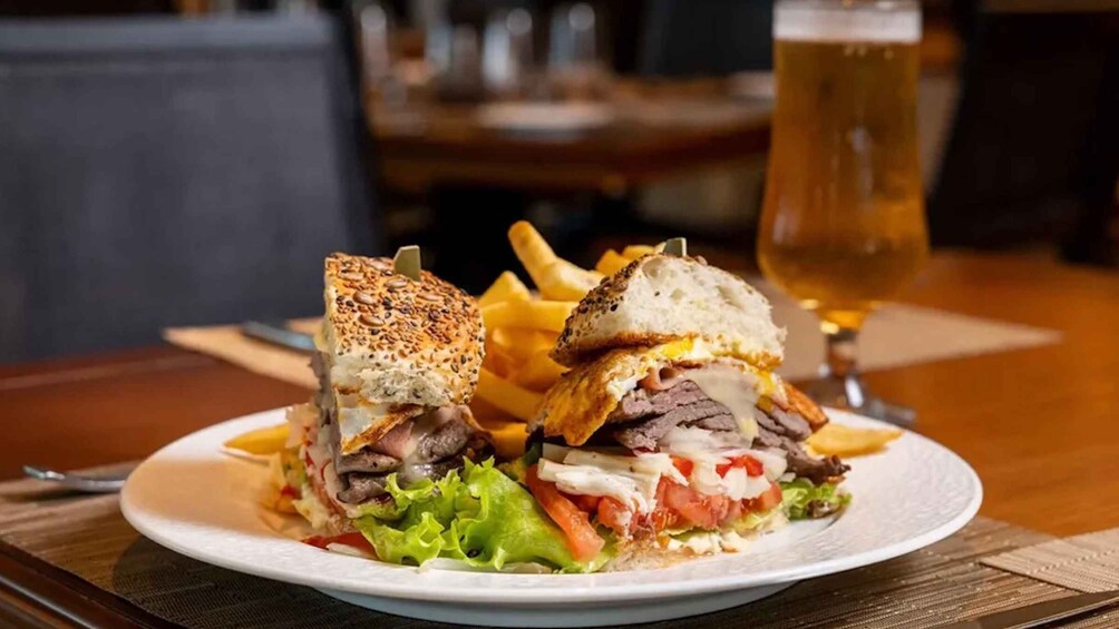 A sandwich with fries and a glass of beer on a table. 1