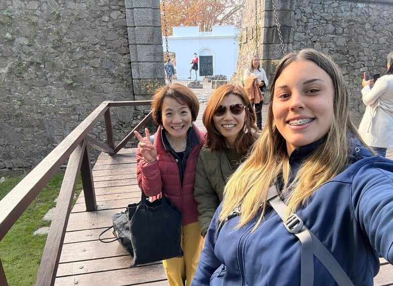 A group of people on a wooden boardwalk with stone walls and a building in the background. 3