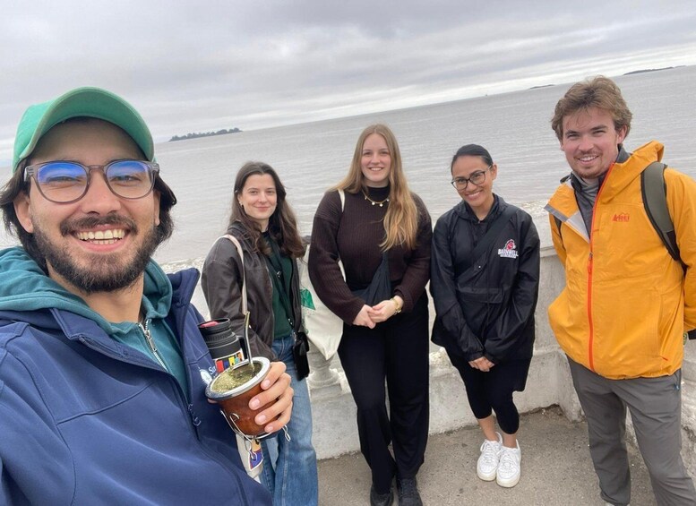 A group of people by a waterfront, one holding a drink. 4