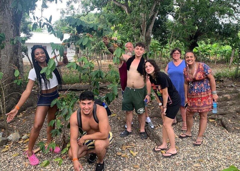 A group of people outdoors, some standing and some crouching, in a natural setting with trees and a gravel ground. 4