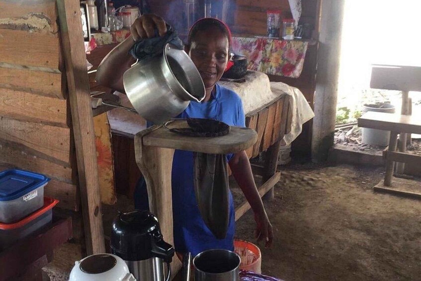 A person pouring a pot into a container on a wooden table in a rustic kitchen setting. 2
