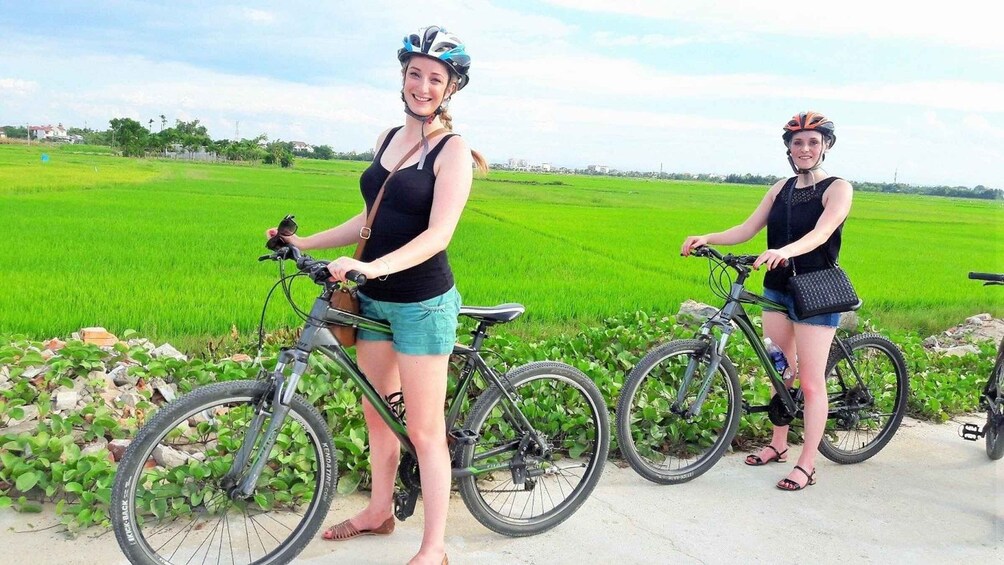 Two people standing next to bicycles in a green field with a clear sky. 5