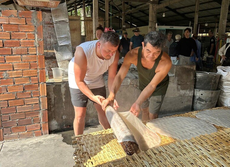 Two men working with a large woven mat and a cylindrical object, possibly a drum, in an industrial setting with brick walls and metal containers. 2