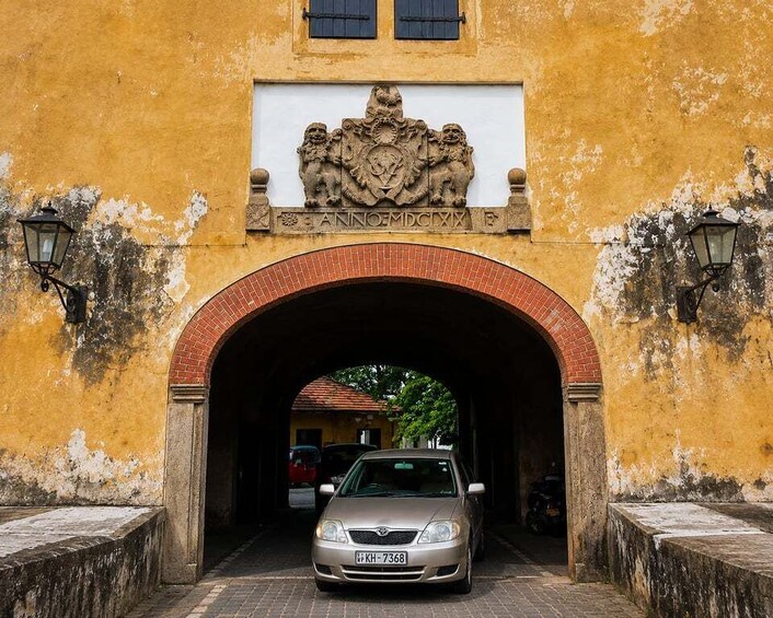 A yellow building with a brick archway, a car, and a coat of arms above the archway. 5