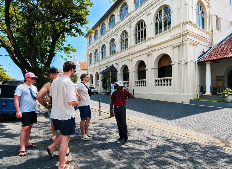 A group of people walking on a cobblestone street in front of a historic building with arched windows and a tiled roof. 2