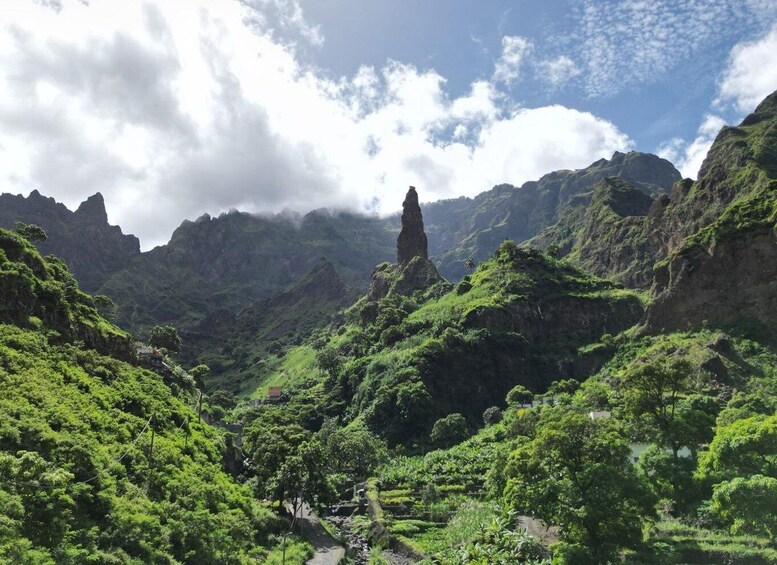 A lush green valley with a prominent rock formation in the center, surrounded by dense vegetation and steep cliffs. 2