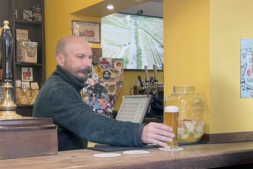 A man at a bar counter with a beer and a large jar of ice cubes. 2