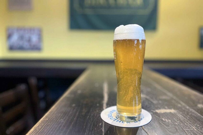 A tall glass of beer on a coaster with 'BREWHEE' text, placed on a wooden table in a bar. 3