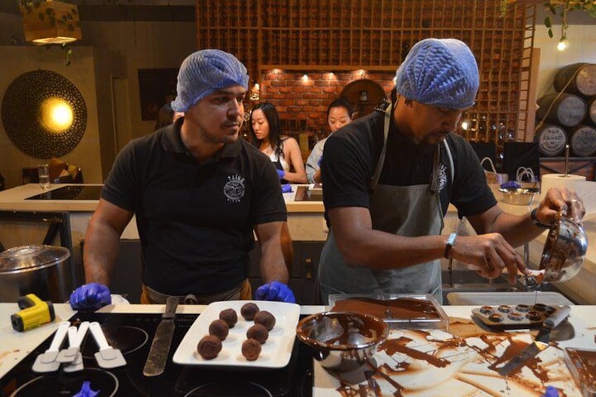 Two chefs in a kitchen preparing food, with a plate of food and a pot on the counter. 1