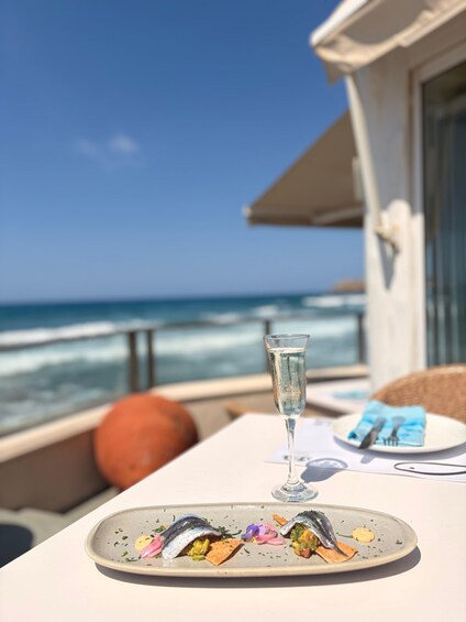 A table with a glass of water and a plate of food on a balcony overlooking the ocean. 5