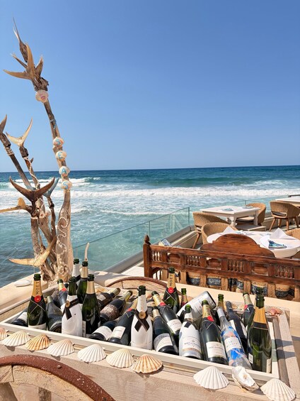 A boat deck with a wooden chair and a table, surrounded by seashells and bottles of champagne. 2