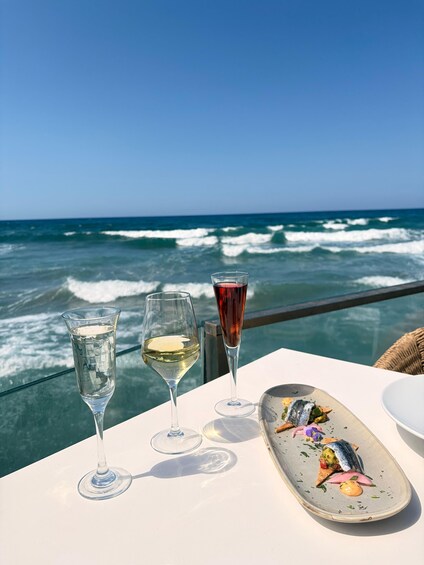 A table with three glasses of wine and a seafood dish by the ocean. 4