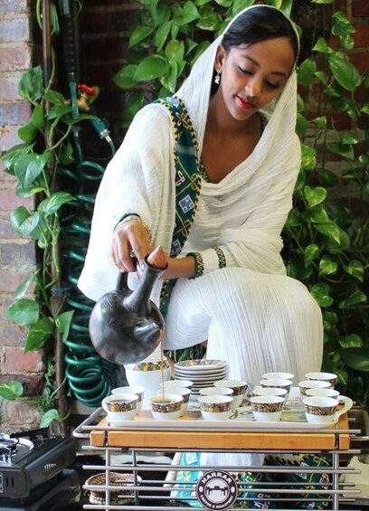A person pouring tea into cups on a tray, surrounded by plants and a brick wall. 2