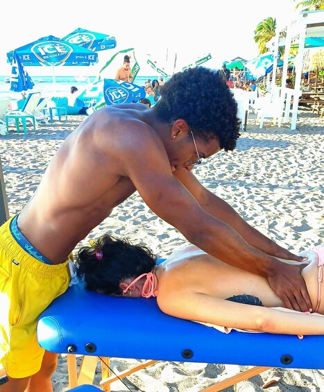 A person receiving a massage on a beach with umbrellas and beach chairs in the background. 1