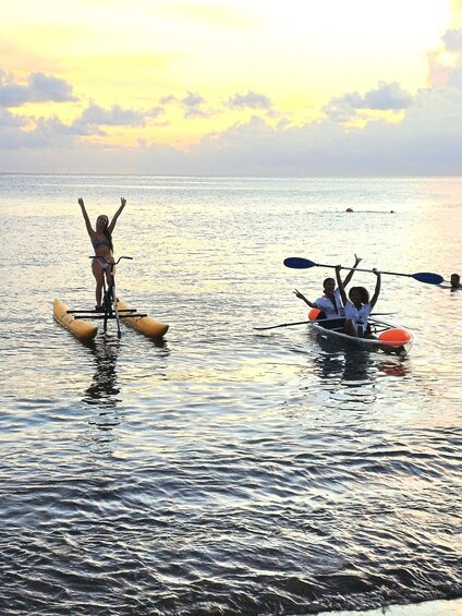 A person standing on a paddleboard in the water, another person paddling a kayak, and a sunset in the background. 5