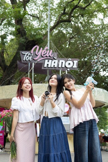 Three women posing in front of a sign with Vietnamese text. 2
