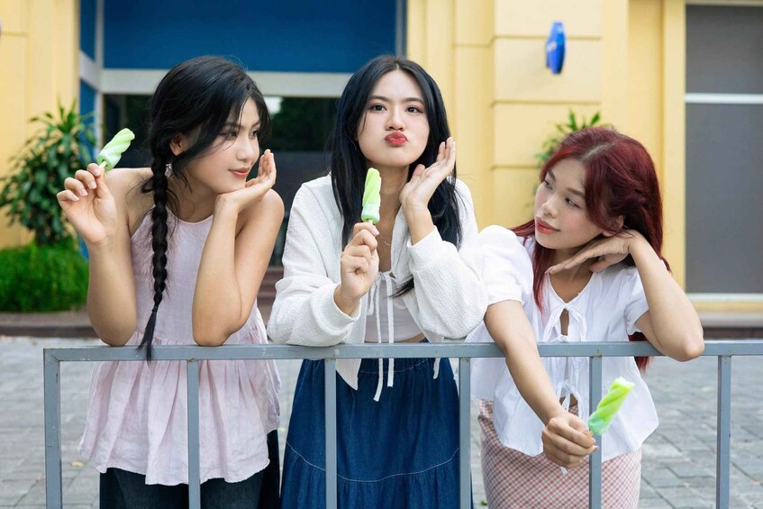 Three individuals leaning on a metal barrier, holding green popsicles. 4